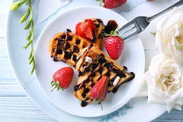 Heart shaped waffles with strawberries and chocolate sauce on plate