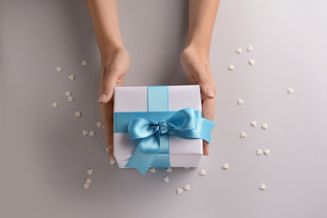 Woman holding gift box with blue ribbon on light background, top view