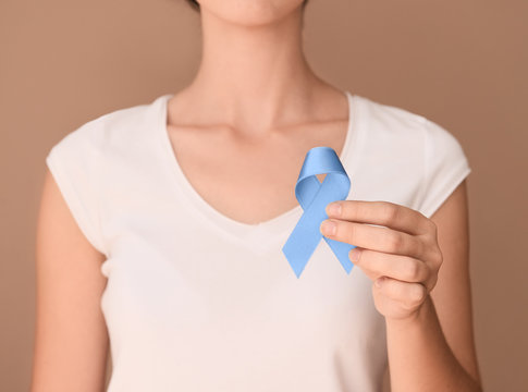 Woman holding blue ribbon on color background. Prostate cancer awareness concept