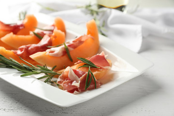 Plate with delicious melon and prosciutto on white wooden table