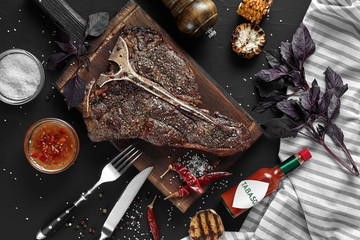 Succulent grilled large t-bone steak garnished with herbs, corn and salt with fork and knife beside...