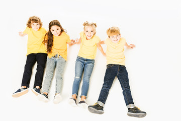 high angle view of adorable happy kids in yellow t-shirts sitting together and smiling at camera isolated on white