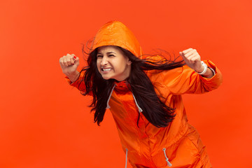 Naklejka premium The young girl posing at studio in autumn jacket isolated on red. Human negative emotions. Concept of the cold weather. Female fashion concepts