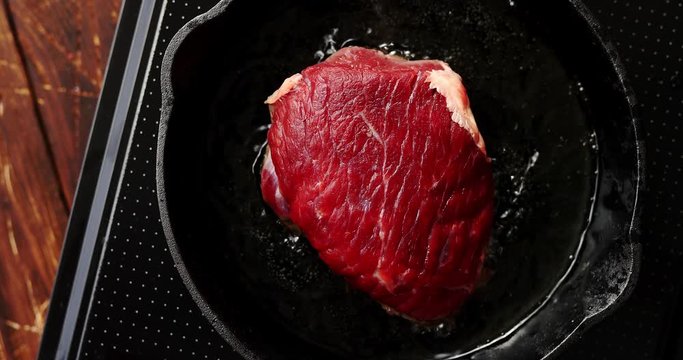From above view of fresh raw meat laid on black pan in process of cooking in oil