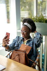 African american female student with frizzy dark hair makes selfie or makes video call, being in high spirit, coming to high shcool classes in time .