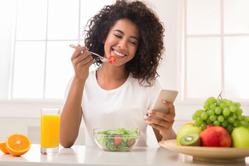 Happy black woman texting on smartphone while eating salad