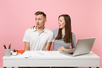 Two young business woman man colleagues sit at white desk isolated on pastel pink background. Sexual harassment, assault lustful boss, intimidation, work ethic, stress, design concept. Co working.