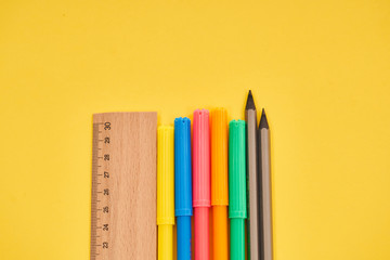 ruler with pencils and colorful pens on yellow background