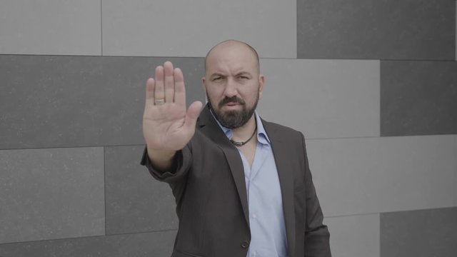Serious business man showing stop hand gesture expressing denial on city street