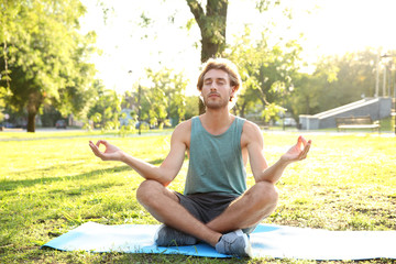 Handsome young man practicing yoga in park