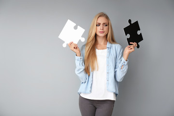 Thoughtful young woman with pieces of puzzle on grey background