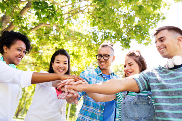 people, friendship and international concept - group of happy smiling friends stacking hands in park