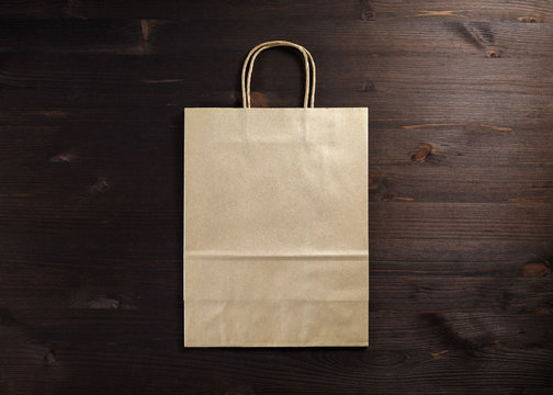 Blank craft paper bag on wooden background. Responsive design mockup. Flat lay.