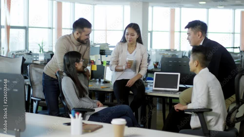 Poster tracking shot of friendly asian colleagues talking to each other when taking break from work in offi