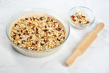 Dough in the form before baking. Put the beans on the dough to maintain the desired shape. Light background. Close-up. 