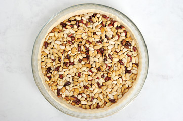Dough in the form before baking. Put the beans on the dough to maintain the desired shape. Light background. Close-up. View from above.