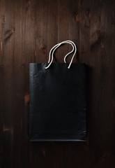 Blank black paper shopping bag with white rope handles on wooden background. Flat lay.