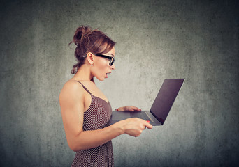 young woman looking at laptop computer screen in misunderstanding and astonishment