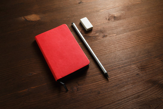 Red notebook, pencil and eraser on wooden background. Template for branding identity.