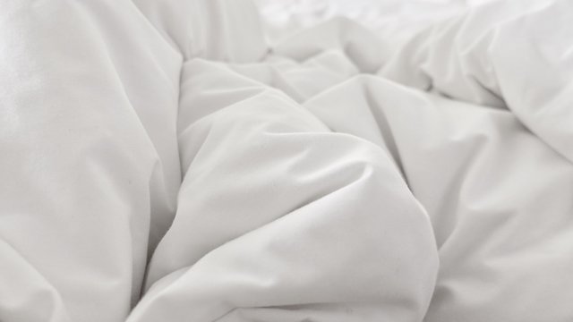 close up top view of white pillow on bed and with wrinkle messy blanket in bedroom, from sleeping in a long night.