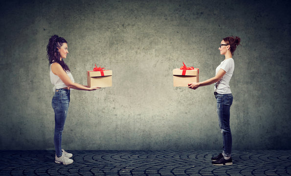 Two women exchanging with gift boxes looking happily at each other