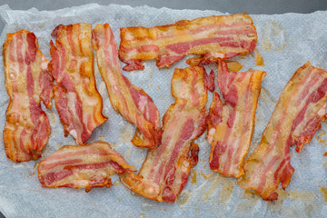 Close-up of appetizing slices of smoked bacon. Isolated on white background. With baking paper. Cooked in the oven, very crispy.