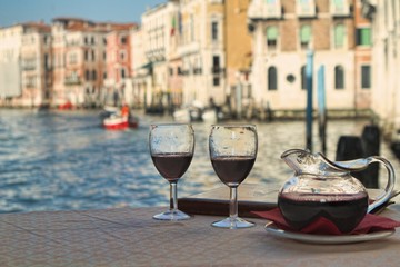 A carafe and two wine glasses filled with red wine sit on a table in front of a leather-bound menu at a restaraunt overlooking the Grand Canal in Venice, Italy