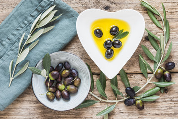 Olive oil bowl and fresh branch of olives on rustic wooden background.