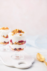 Healthy raspberry yogurt parfait in a glass with golden spoon on white marble table over pink background with copy space.