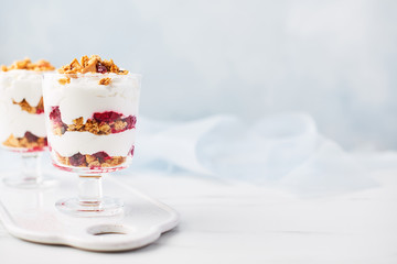 Healthy raspberry yogurt parfait in a glass on white marble table over light blue background with copy space.