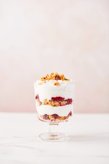 Healthy raspberry yogurt parfait in a glass on white marble table over pink background with copy space.