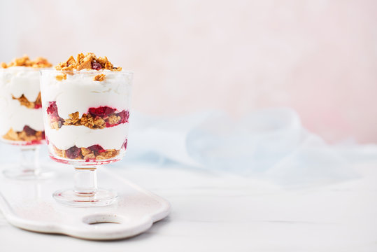 Healthy raspberry yogurt parfait in a glass on white marble table over pink background with copy space.
