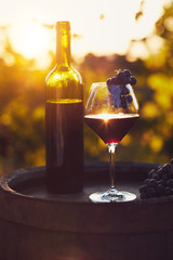 A glass of red wine with on a wooden barrel at sunset