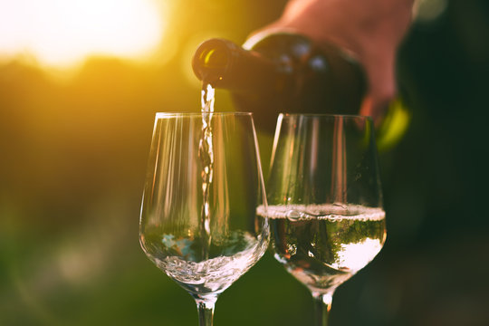 Naklejka Pouring white wine into glasses at sunset
