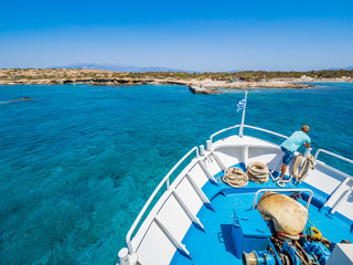Greek flag waving on the bow of a boat sailing toward the island of Chrissi. The uninhabited island...