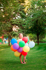 Happy little girl playing with large bunch of helium filled colorful balloons