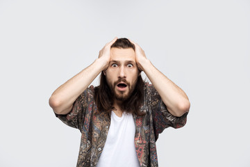 Indoor shot of puzzled and confused man with bristle scratching head and opening mouth while looking at camera and standing over white background. Problems at work and an error while performing