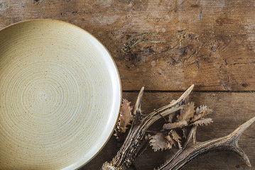 Hunting still life: empty plate and deer antlers on dry oak leaves and vintage wooden background with copy space