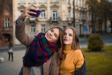 Close up lifestyle portrait of two pretty fresh hipster young teenage girls. Best friends girls,make selfie and having fun. Cute pretty girls making funny selfie on the street, having fun together. 