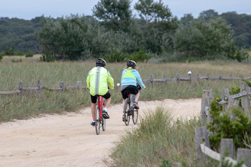 couple biking on a path in a park with trees, grass and a fence