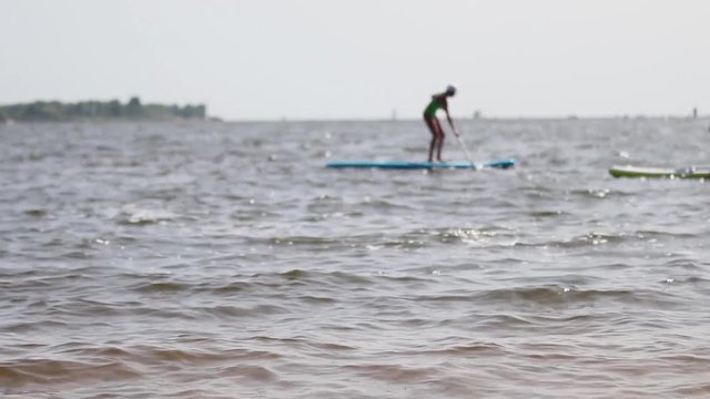 A long establishing shot of a stand-up paddle boarder SUP on the river out of focus. Concept of water tourism. Beautiful summer vacation background. 