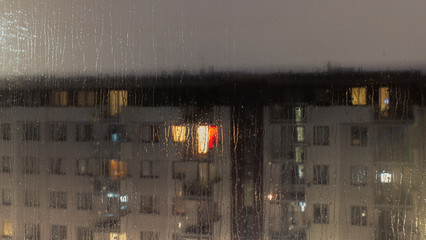 Rainy evening and the view of the rain-covered glass through which you can see a fuzzy block of flats