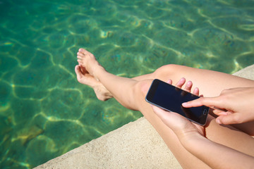 A woman holding smartphone while sitting on the seaside pier.