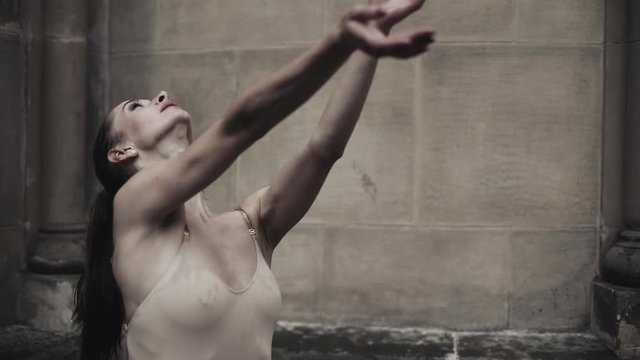 Young professional female dancers is performing acrobatic dance along the medieval street under the rain. Wet girls dancing in water drops, slow motion