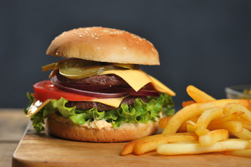 Double cheeseburger and french fries on a light wooden table. Burger filling consists of two steaks, vegetables, cheese and sauce. Dark background. Close-up. Macro shooting.