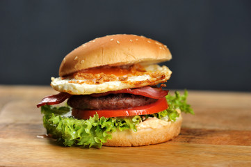 Hamburger on a light wooden surface. The burger includes bacon, fried egg and dried onions. Close-up. Macro shooting.
