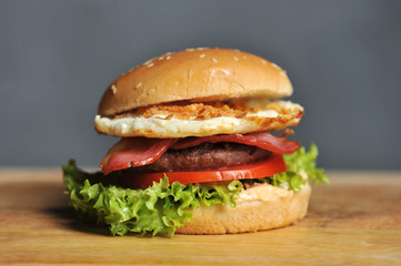 Hamburger on a light wooden surface. The burger includes bacon, fried egg and dried onions. Close-up. Macro shooting.