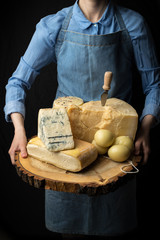 Rustic gourmet italian cheese on wooden board in hands of cheese maker on black background