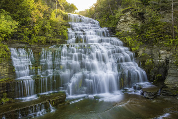 Obraz premium Beautiful sunrise over Hector Falls at Watkins Glen, upstate New York, featuring sun beaming trough the trees on the background