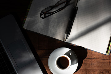 Woodgrain Table with Computer, espresso coffee in a white cup on a white saucer, Glasses, Pen and Notebook.
